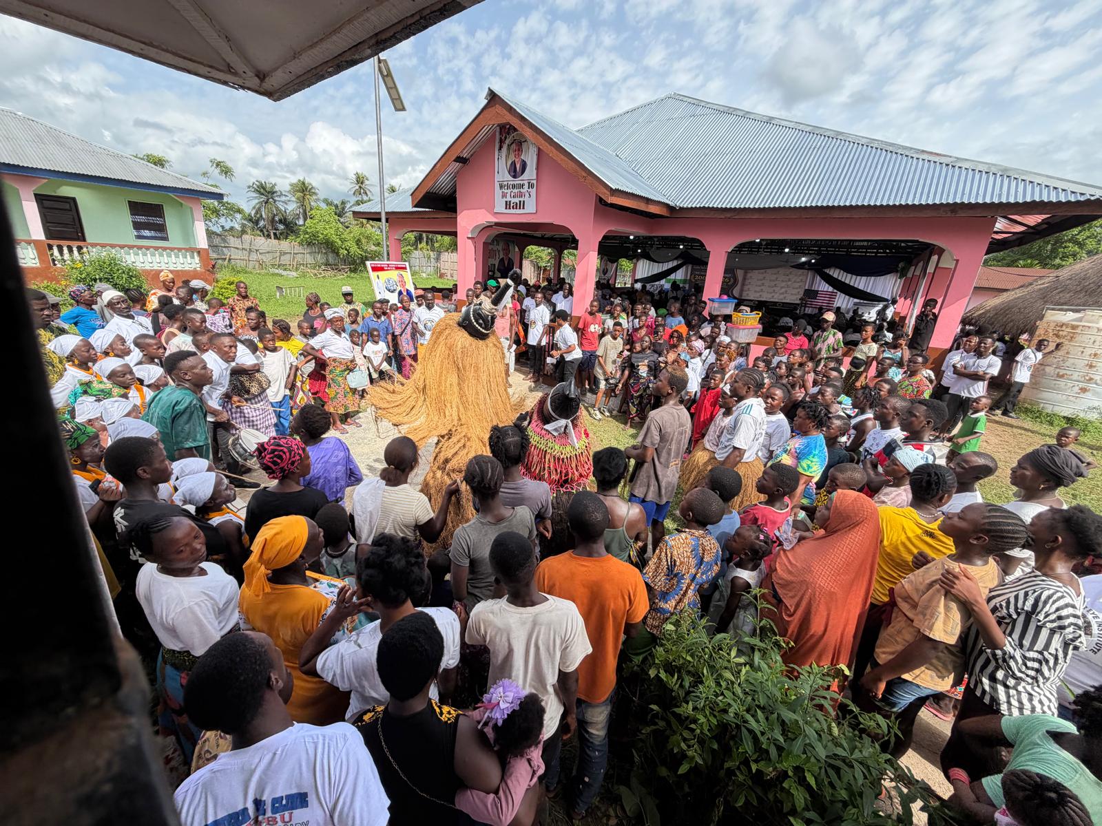 Traditional dancer surrounded by community crowd outside Dr. Cathy's Hall at the 20th Anniversary